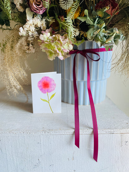 Vase of flowers with a card featuring a pink flower on a white surface
